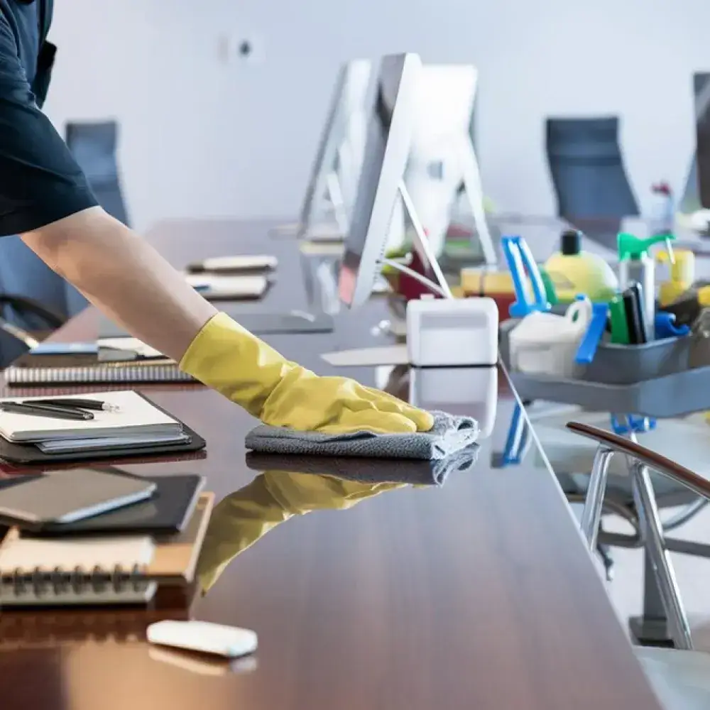 Cleaner performing office cleaning around desks and glass doors before employees arrive